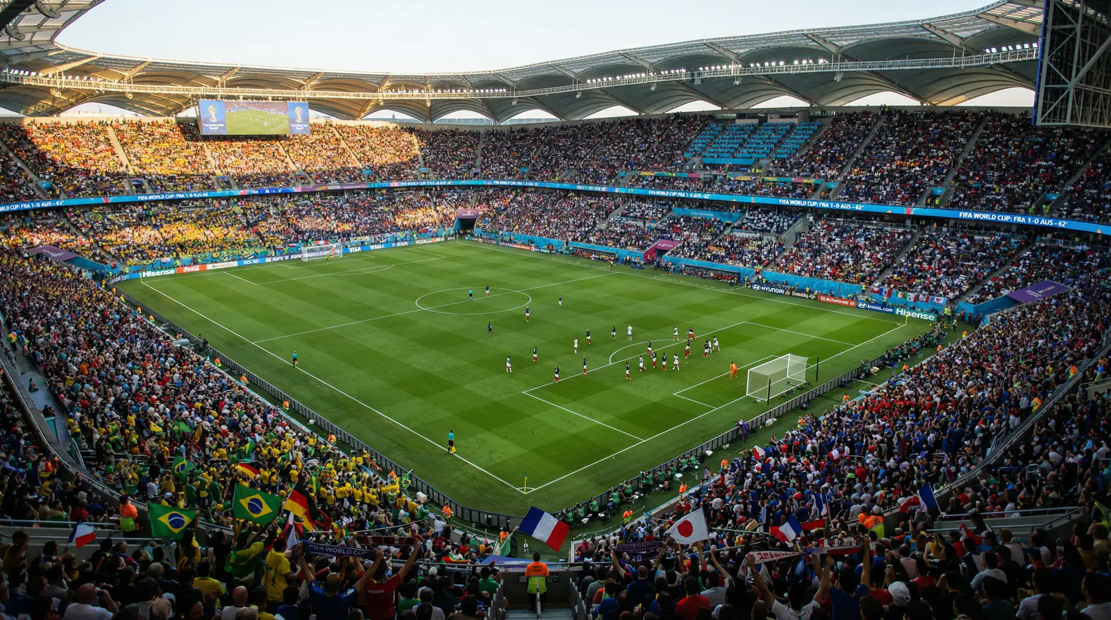 Fullsatt fotbollsstadion under ett VM-gruppspel med nationsflaggor från flera länder i publikhavet